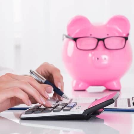 Person Calculating Bill With Pink Piggybank On Desk