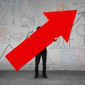 Man Holding Red Arrow Pointing Upward with Graphs and Charts Behind Him on Wall