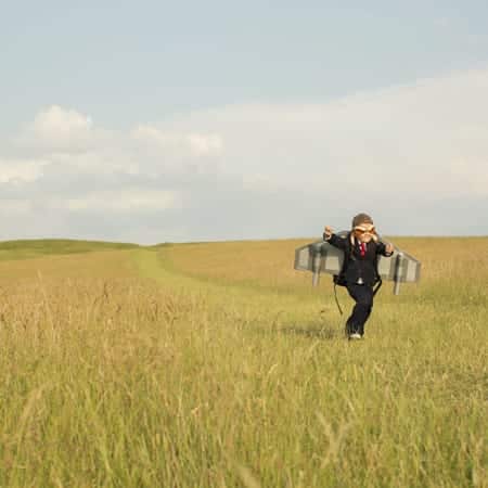 little boy dressed in suit with rocket running in a field