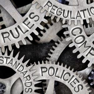 Macro photo of tooth wheels with COMPLIANCE, REGULATIONS, STANDARDS, POLICIES and RULES words imprinted on metal surface